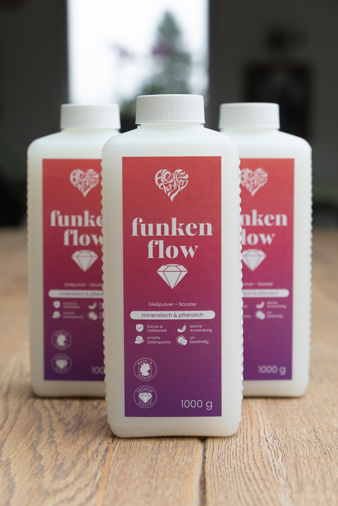 Drei Flaschen Funkenflow Gießpulver-Booster nebeneinander auf einem Holztisch präsentiert.